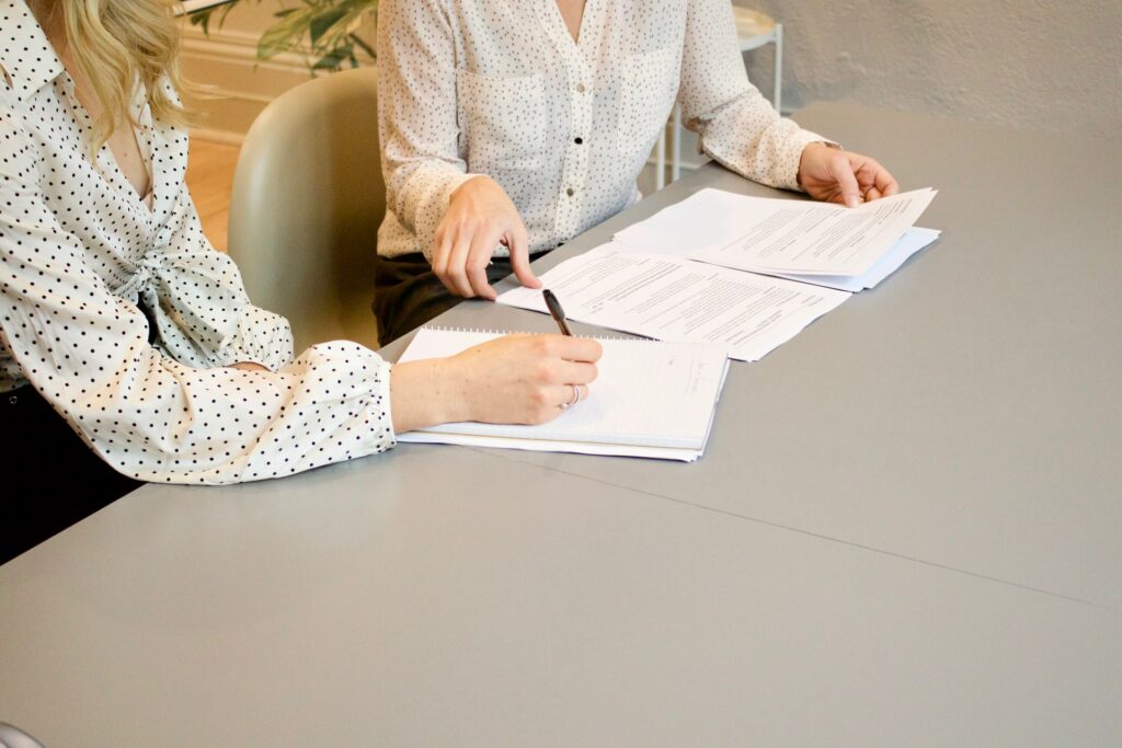 two women sitting on desk signing documents needed to sell land by owner