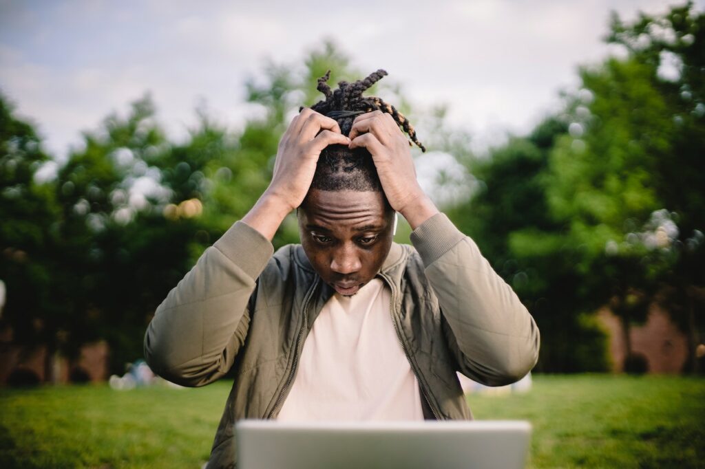 Stressed african-american male about selling of land online on laptop in park