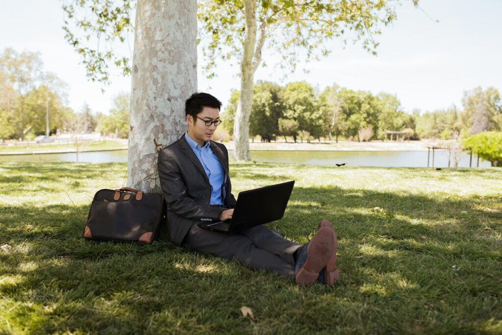 man leaned on tree selling vacant land on his lap top