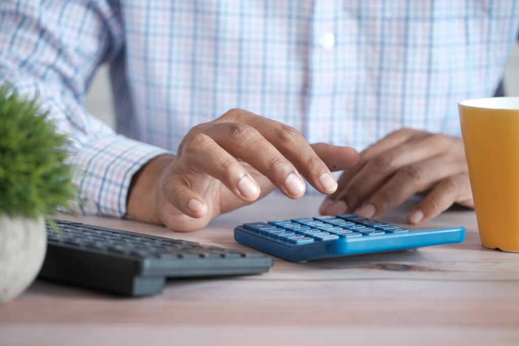 Man's hands typing on calculator to estimate how to sell land without paying taxes