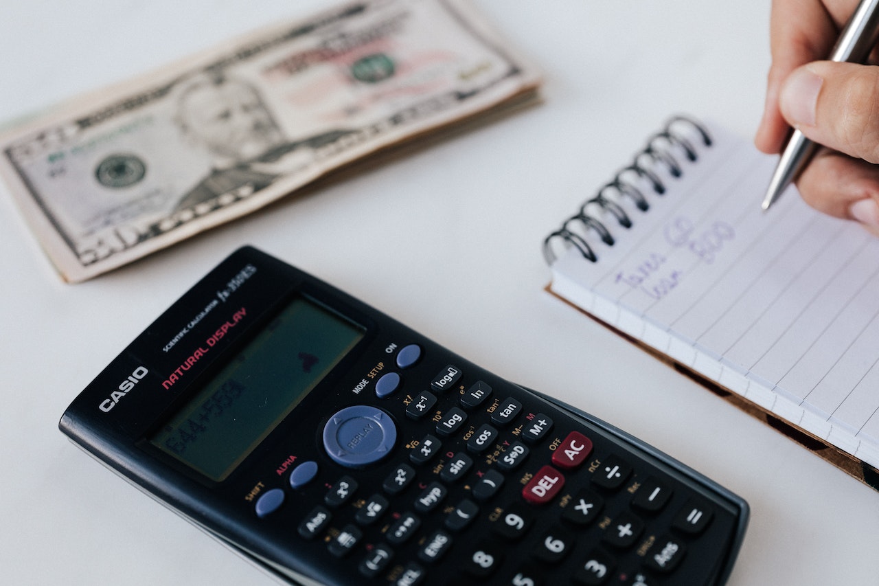 A person who buys land considering if a vacant lot is worth purchasing by doing written estimates next to a calculator and American dollars on a white table